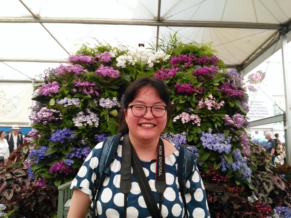 Piangfan standing with blue flowered shrub in the background Piangfan standing with blue flowered shrub in the background